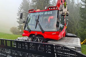Rote Pistenraupe der Bergbahn Söll an einem vernebelten Tag mit Tannen im Hintergrund
