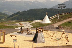 Ein Spielplatz in den Bergen mit Klettergerüst, Schaukeln und einem Tipi. Berglandschaft im Hintergrund, ideal für Outdoor-Aktivitäten.