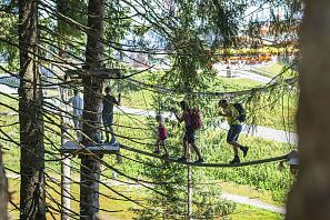 Familie und Freunde überqueren eine Hängebrücke zwischen Bäumen in einem Wald.