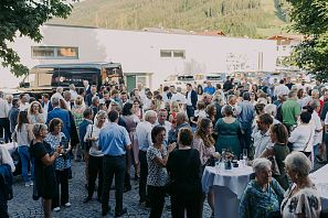Menschenmenge bei einer Outdoor-Veranstaltung mit Stehtischen, Catering im Hintergrund, sommerliche Atmosphäre.