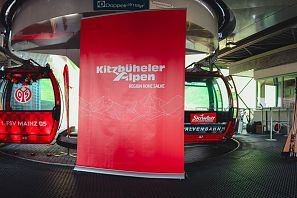 Zwei Gondeln der Seilbahn Kitzbüheler Alpen stehen in einer Station neben einem großen Werbebanner.