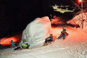 Fünf Personen rodelnd auf der beleuchtenden Rodelbahn Hexenritt in Söll am Abend