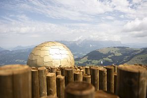 Een gouden bol op een houten omheining met bergachtig landschap op de achtergrond.