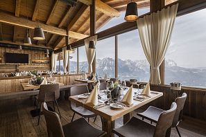 Das stilvoll gedecktes Bergrestaurant Kaiserlounge am Hartkaiser mit großen Panoramafenstern, durch die ein beeindruckender Blick auf das majestätische Kaisergebirge fällt. Die Einrichtung aus Holz schafft eine gemütlich-alpine Atmosphäre