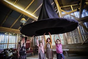 Kinder stehen gemeinsam mit freundlicher Hexe unter riesigen Hexenhut im Gebäude "Hexerei" in der ErlebnisWelt Hexenwasser in Söll