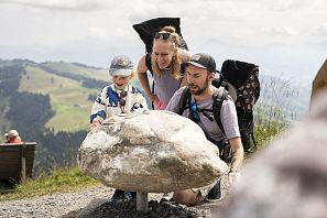 Een gezin met een kind dat een grote steen op een berg bekijkt tijdens een wandeling.