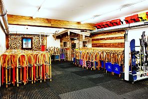 In einem modernen Skiraum sind zahlreiche Ski und Snowboards ordentlich aufgereiht. Die Wände sind teilweise mit Holz verkleidet, und die Atmosphäre wirkt gemütlich und einladend.