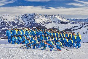 Gruppe von Skifahrern in blauen Outfits vor schneebedeckten Bergen.