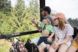 Familie fährt in einer Seilbahn und schaut nach draußen auf die grüne Landschaft.