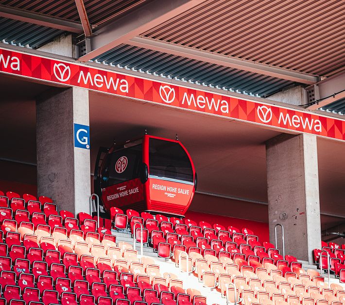 Eine Gondel in einem Stadion mit roten Sitzplätzen und Werbung im oberen Bereich.
