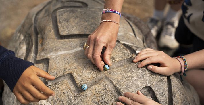 Hands interacting with carved stone and marbles in an outdoor setting.