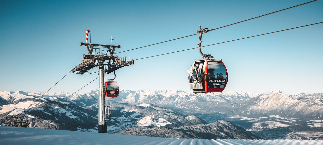 Seilbahn über schneebedeckte Berge, mit klar blauem Himmel und einer atemberaubenden, verschneiten Landschaft im Hintergrund.
