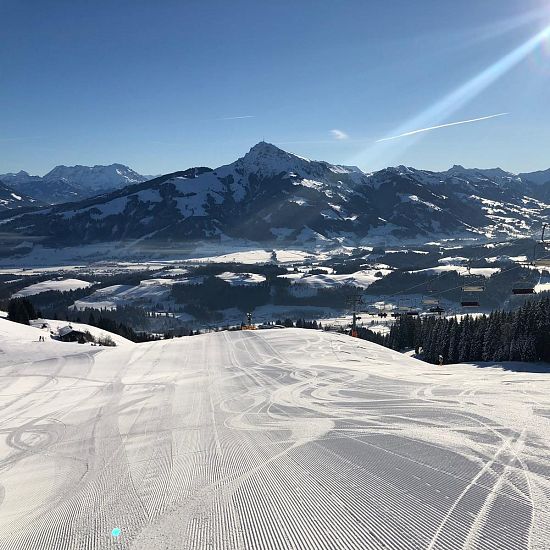 Talabfahrt Astberg mit präparierter Piste, Sonnenschein und Blick auf das verschneite Tal vor dem Kitzbühler Horn