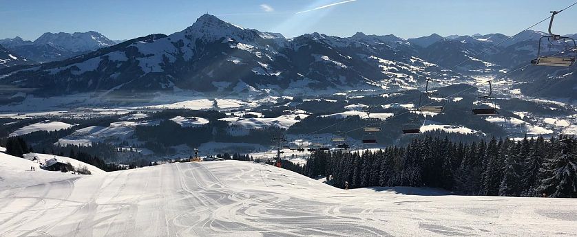 Talabfahrt Astberg mit präparierter Piste, Sonnenschein und Blick auf das verschneite Tal vor dem Kitzbühler Horn