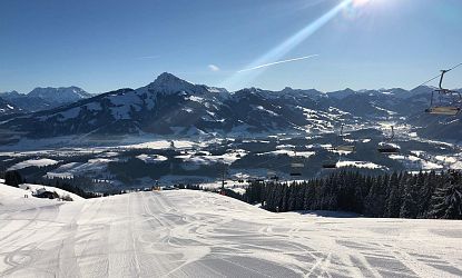 Talabfahrt Astberg mit präparierter Piste, Sonnenschein und Blick auf das verschneite Tal vor dem Kitzbühler Horn