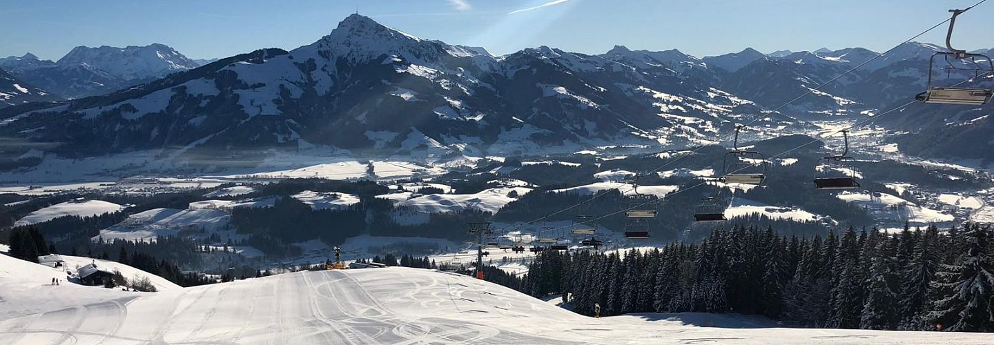 Talabfahrt Astberg mit präparierter Piste, Sonnenschein und Blick auf das verschneite Tal vor dem Kitzbühler Horn