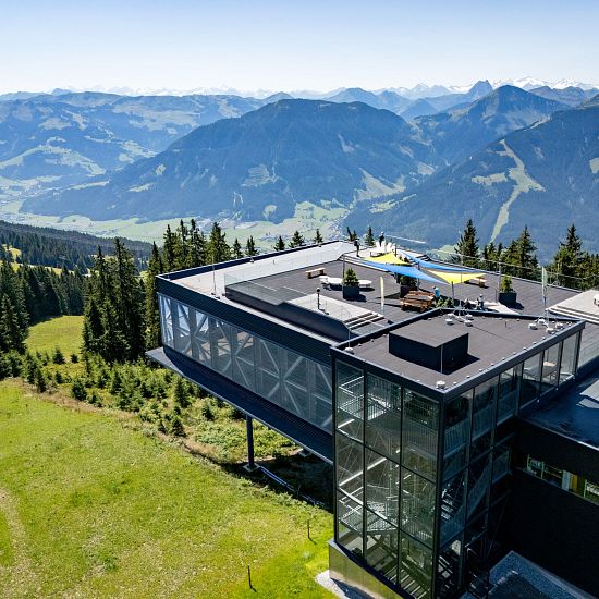 Riesen-Panorama-Aussichtsplattform mit Glasfassade und Dachterrasse, umgeben von Bergen und Wäldern.
