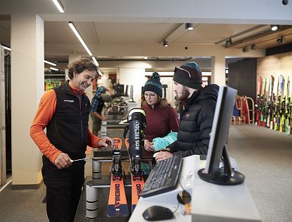 Gäste werden von einem Mitarbeiter zu Skiern beraten.