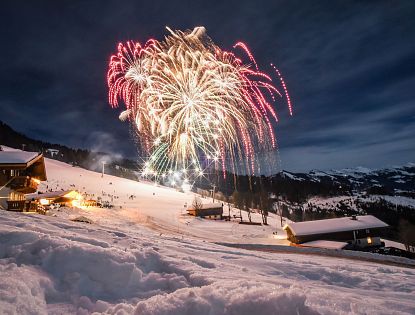 Feuerwerk über verschneiter Winterlandschaft in Hopfgarten mit beleuchteten Skihütten und Piste bei Nacht