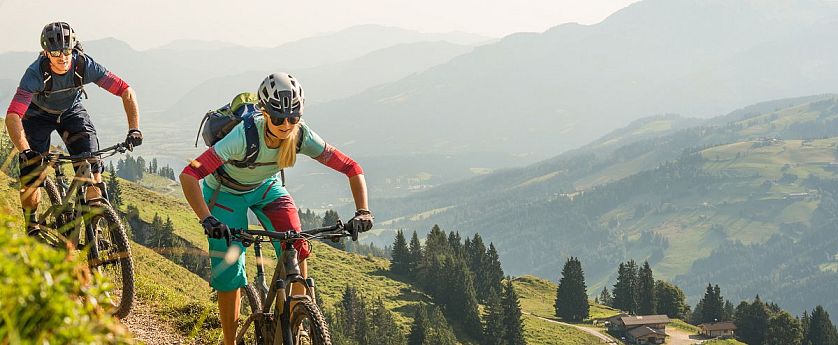 Zwei Mountainbiker im Sommer mit Rucksack, Helm und Brille am Wiegalmtrail mit leicht vernebeltem Panoramablick