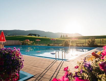 Poolanlage im Sommer in Naturlandschaft mit violetten Blumen und roten Eskimo Sonnenschirmen
