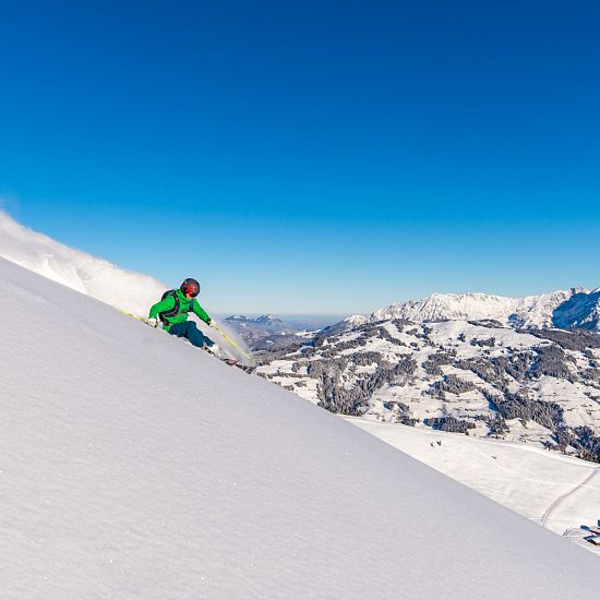Freerider mit grüner Jacke im frischen Pulverschnee zieht erste Spuren mit Panoramablick im Hintergrund