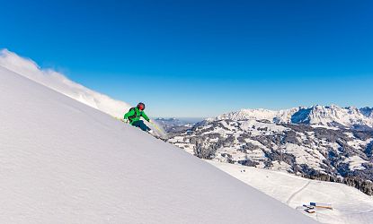 Freerider mit grüner Jacke im frischen Pulverschnee zieht erste Spuren mit Panoramablick im Hintergrund