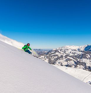 Freerider mit grüner Jacke im frischen Pulverschnee zieht erste Spuren mit Panoramablick im Hintergrund