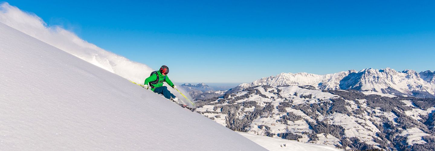 Freerider mit grüner Jacke im frischen Pulverschnee zieht erste Spuren mit Panoramablick im Hintergrund