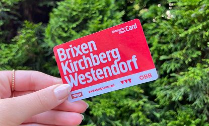 Frauenhand hält Gästekarte Kitzbuehler Alpen mit Aufschrift Brixen Kirchberg Westendorf