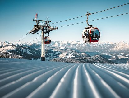 Seilbahn über schneebedeckte Berge, mit klar blauem Himmel und einer atemberaubenden, verschneiten Landschaft im Hintergrund.