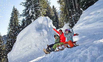 Familie rodelt auf der Rodelbahn Hexenritt in Söll mit gehobenen Armen und fröhlichen Gesichtern