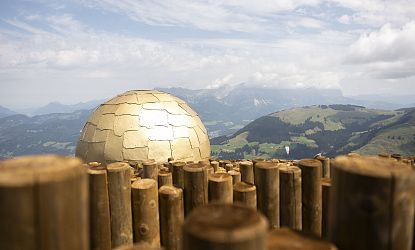 Golden dome on mountain peak with wooden posts and distant hills under a cloudy sky.