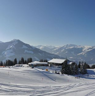 Verschneite Winterlandschaft mit Pisten, Berghütten, Skifahrern und strahlender Sonne über dem Skigebiet Wilder Kaiser – Brixental