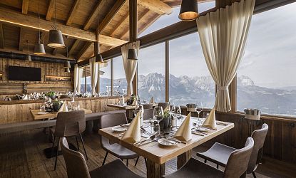 Das stilvoll gedecktes Bergrestaurant Kaiserlounge am Hartkaiser mit großen Panoramafenstern, durch die ein beeindruckender Blick auf das majestätische Kaisergebirge fällt. Die Einrichtung aus Holz schafft eine gemütlich-alpine Atmosphäre