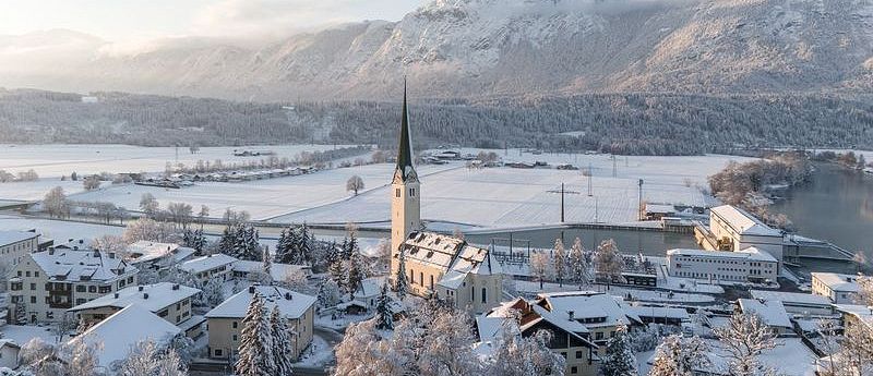 Verschneite Ortschaft Kirchbichl im Winter mit Sonnenstrahlen welche auf den Ort eintreffen