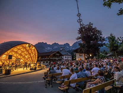 Platzkonzert im Musikpavillon vor Bergkulisse des Wilden Kaisers in Tirol mit zahlreichen Besuchern bei Sonnenuntergang in Going.