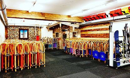 In einem modernen Skiraum sind zahlreiche Ski und Snowboards ordentlich aufgereiht. Die Wände sind teilweise mit Holz verkleidet, und die Atmosphäre wirkt gemütlich und einladend.
