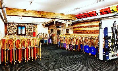 In einem modernen Skiraum sind zahlreiche Ski und Snowboards ordentlich aufgereiht. Die Wände sind teilweise mit Holz verkleidet, und die Atmosphäre wirkt gemütlich und einladend.
