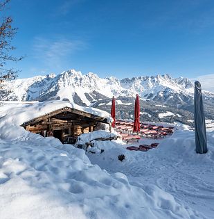 Beschneite Hütte am Berg mit einem Alpenpanorama.