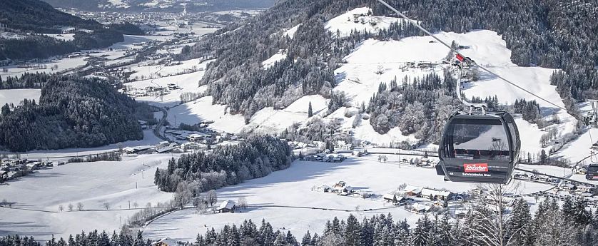 Lanovka nad zasněženou horskou krajinou s lesy a chatami, zasněžené stromy a kopce v zimní scenérii.