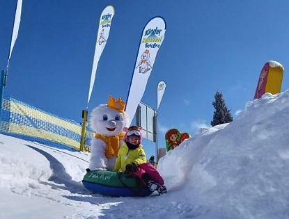 Kind beim Snowtubing im KinderKaiserland Scheffau mit Maskottchen im Schnee, Winterspaß und Familienerlebnis in der SkiWelt Wilder Kaiser Brixental.