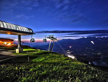 Brandstadl Bergstation in der Nacht mit Blick zum Wilden Kaiser, im Hintergrund das Sonnwendfeuer zu sehen