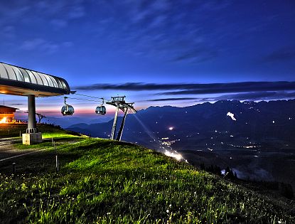 Brandstadl Bergstation in der Nacht mit Blick zum Wilden Kaiser, im Hintergrund das Sonnwendfeuer zu sehen