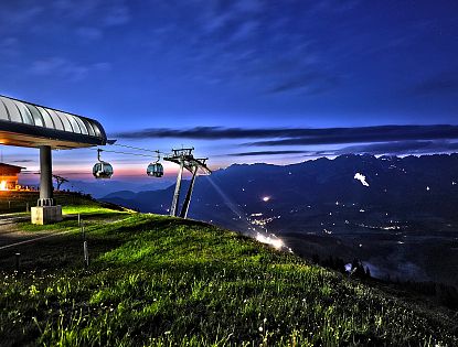 Brandstadl Bergstation in der Nacht mit Blick zum Wilden Kaiser, im Hintergrund das Sonnwendfeuer zu sehen
