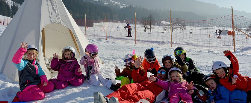 Kinder im Skikurs mit Skilehrer im Schnee in der SkiWelt Wilder Kaiser Brixental, spielerisches Skifahren und Spaß im Schnee vor einem Tipi.