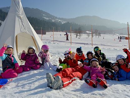 Kinder im Skikurs mit Skilehrer im Schnee in der SkiWelt Wilder Kaiser Brixental, spielerisches Skifahren und Spaß im Schnee vor einem Tipi.