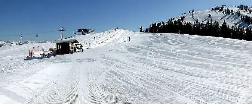 Perfekt präparierte Skipiste mit Übungslift am Brandstadl im sonnigen Skigebiet bei strahlend blauem Himmel.