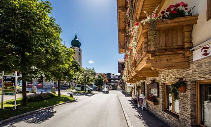 Ortszentrum Westendorf im Sommer, Haus direkt an der Straße mit bunten Blumen die vom Balkon hängen zusehen