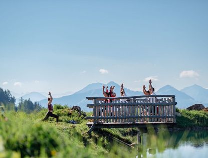 Yoga-Gruppe am Bergsee auf der kleinen Salve in der SkiWelt Wilder Kaiser – Brixental mit Blick auf die Alpen im Sommer.